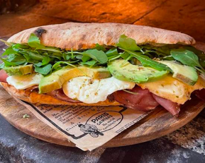 Panuozzo Speck : Pain cuit au feu de bois, farine Label Rouge, base sauce tomate, speck di montagna (IGP), roquette BIO, mozzarella "FDT", avocat.